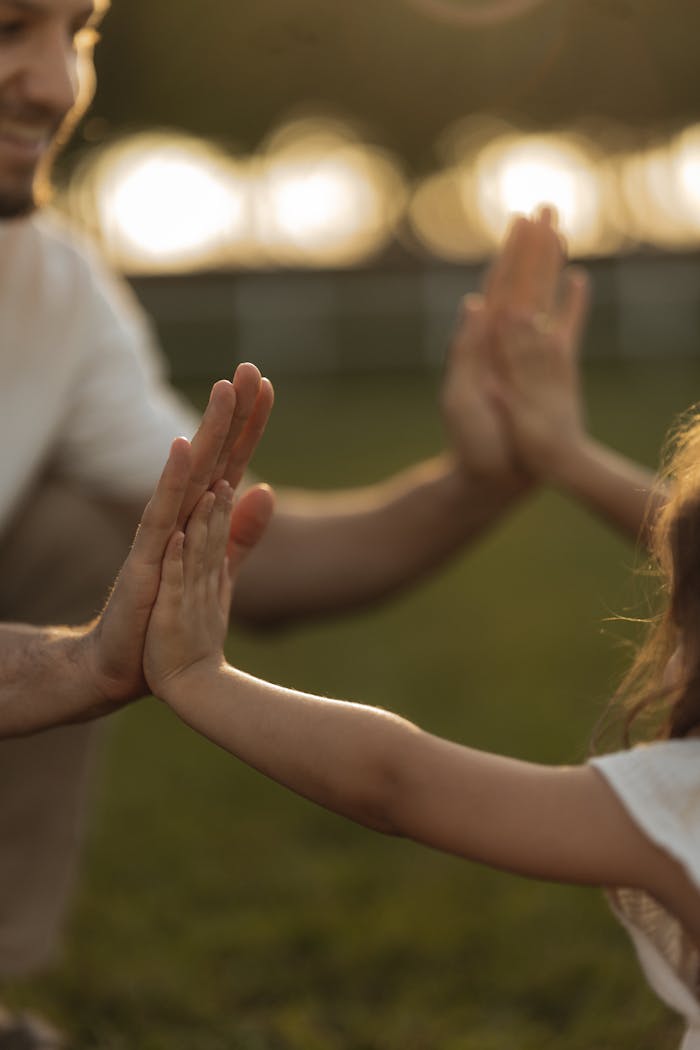 A touching moment of a father and child high-fiving outdoors during sunset.
