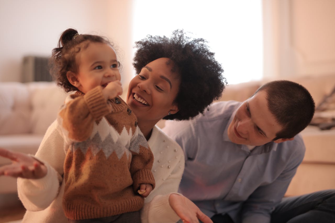 A joyful family bonding moment with parents and toddler in a cozy living room setting.